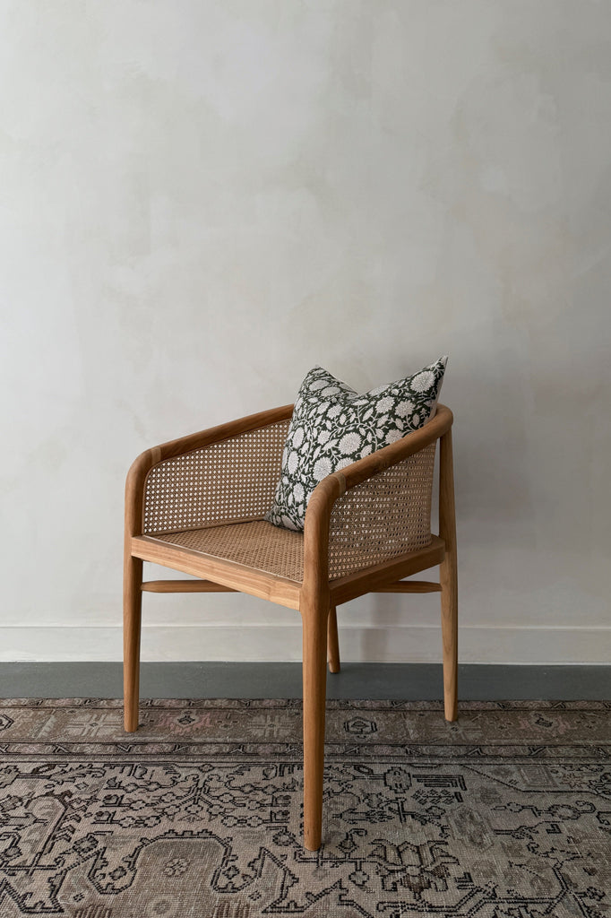 Rattan accent chair with a patterned pillow against a plain wall