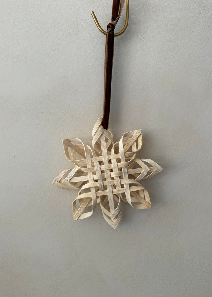 Woven rattan snowflake ornament hanging on a brown ribbon against a limewash background