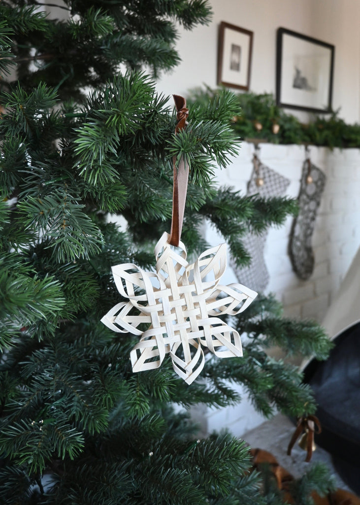Woven rattan snowflake ornament on a Christmas tree with stockings in the background