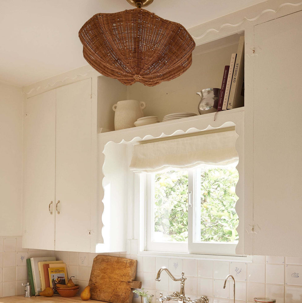 Kitchen interior with wicker Ravello Flushmount light fixture, window, and white cabinets.