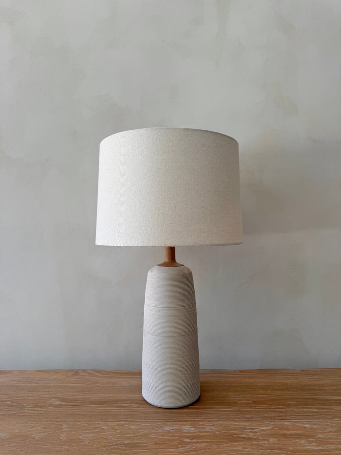 Ravello Ceramic Table Lamp in Ivory with oatmeal linen shade on a white oak table against a limewashed wall. - Saffron + Poe