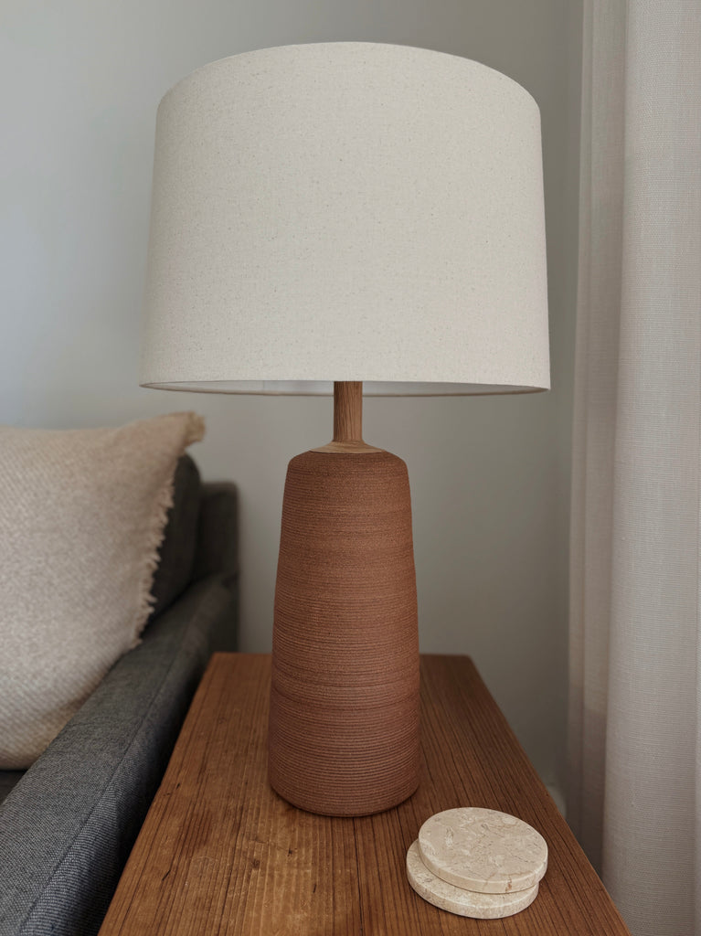 Ravello Ceramic Table Lamp in Terracotta with oatmeal linen shade on a wooden vintage table next to a blue sofa. - Saffron + Poe