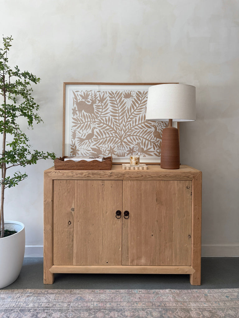 Ravello Ceramic Table Lamp in Ivory with oatmeal linen shade on a vintage wooden cabinet styled with decorative items. - Saffron + Poe