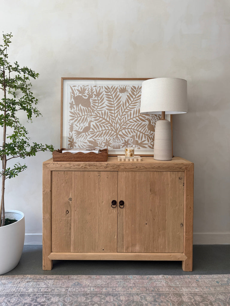 Ravello Ceramic Table Lamp in Ivory with oatmeal linen shade on a vintage wooden cabinet styled with decorative items. - Saffron + Poe