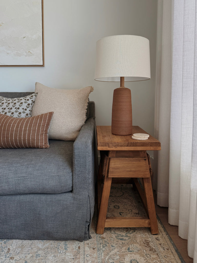 Ravello Ceramic Table Lamp in Terracotta with oatmeal linen shade on a wooden vintage table next to a blue sofa. - Saffron + Poe