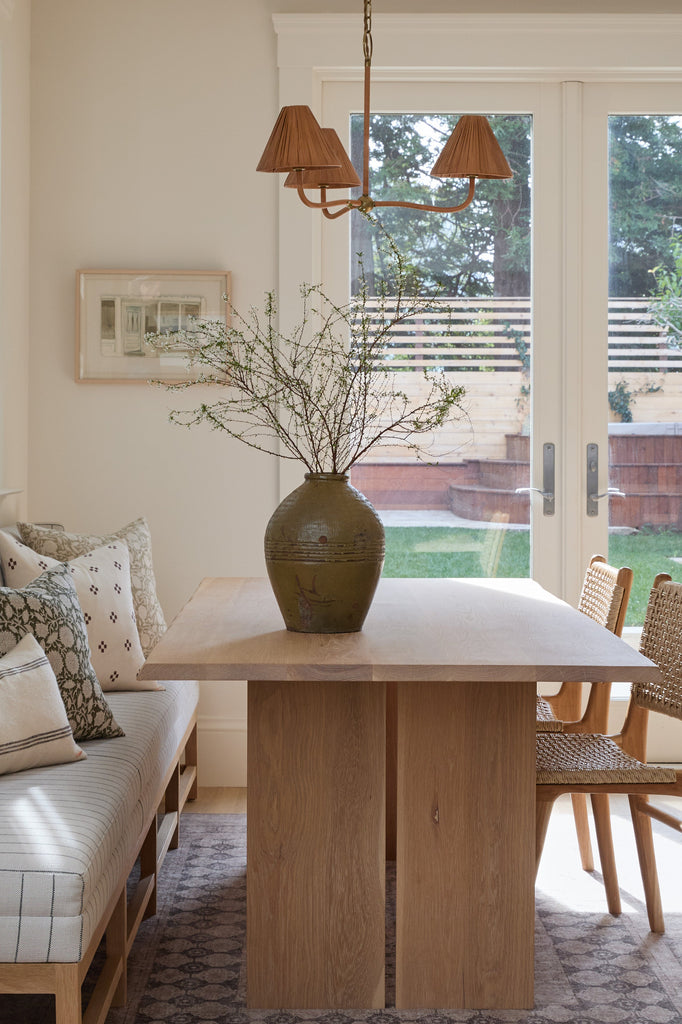 Dining room with wooden table, chairs, and a vase with branches.