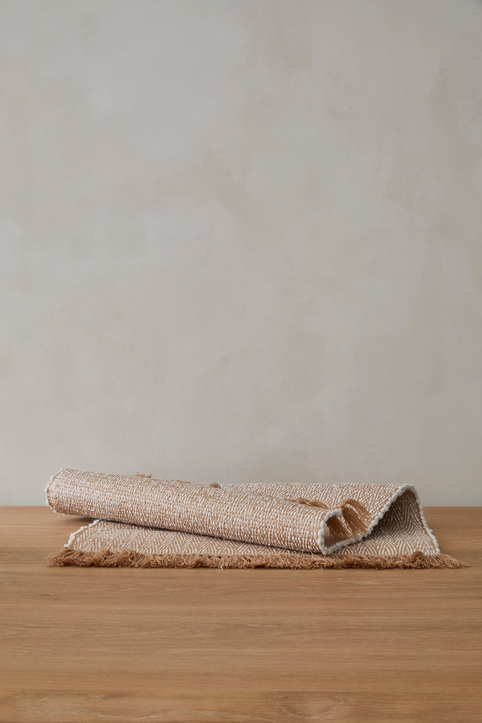 Handwoven bath mat on a wooden surface with a plain background