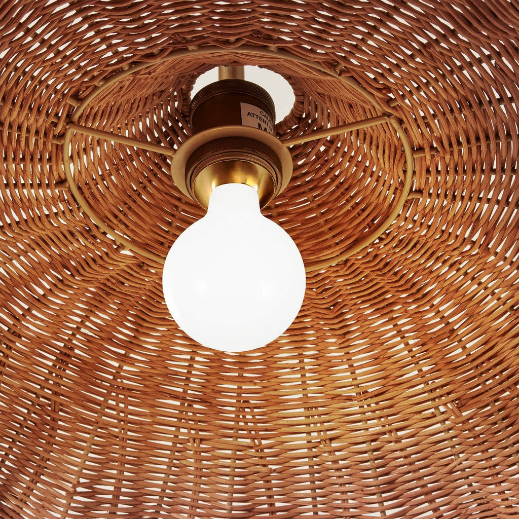 A close-up view from below looking up at the Savannah large wicker pendant light fixture with a glowing white globe bulb and brass-colored metal hardware.