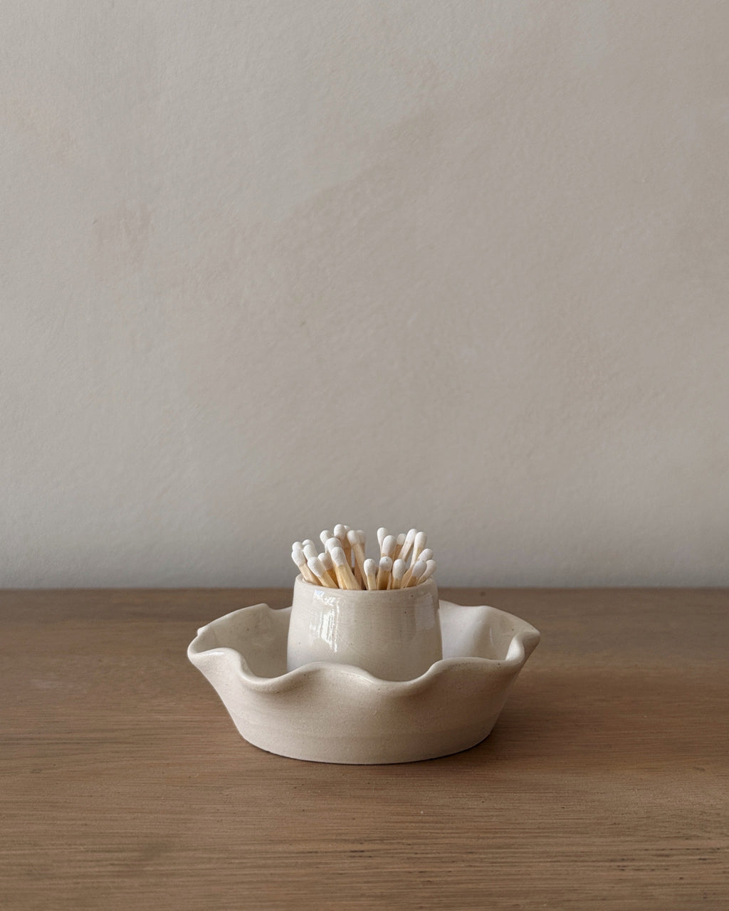 Scalloped ceramic match holder with matches on an oak table.