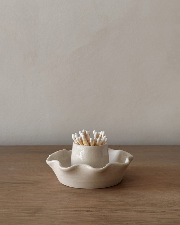 Scalloped ceramic match holder with matches on an oak table.