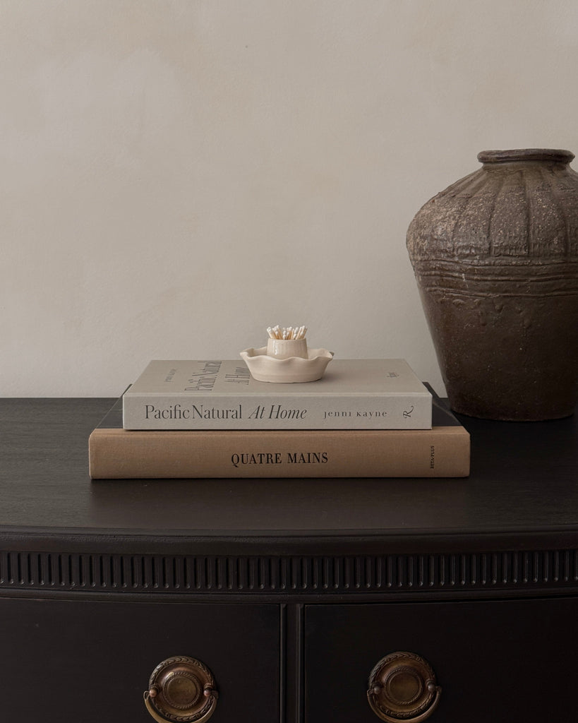 Two books stacked on a dark surface with a textured vase in the background.
