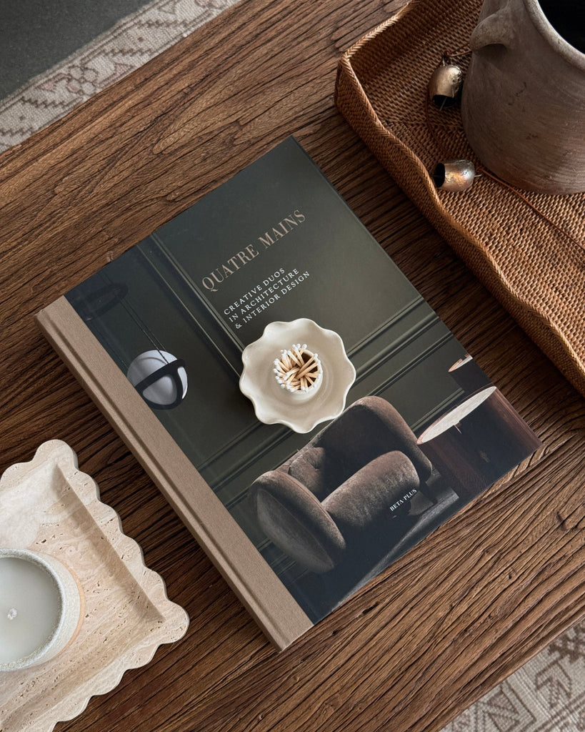Book titled 'Quatre Mains' on a wooden surface with decorative items.