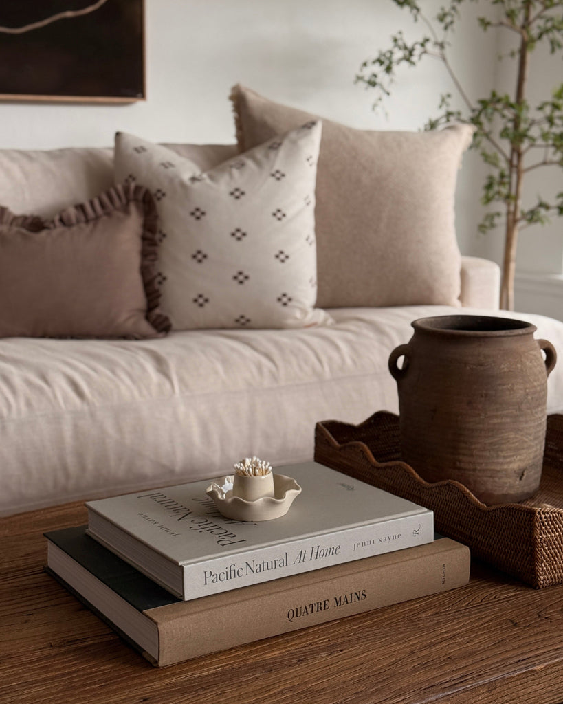 Cozy living room with a beige sofa, decorative pillows, and a wooden coffee table with books and a vase.