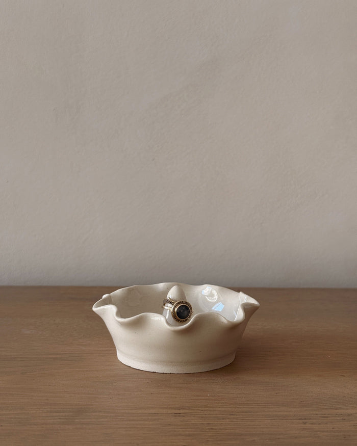 White ceramic dish with scalloped edge on a wooden surface against a beige wall