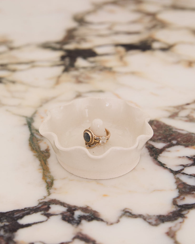 Gold ring with a blue stone on a white ceramic dish against a marble background