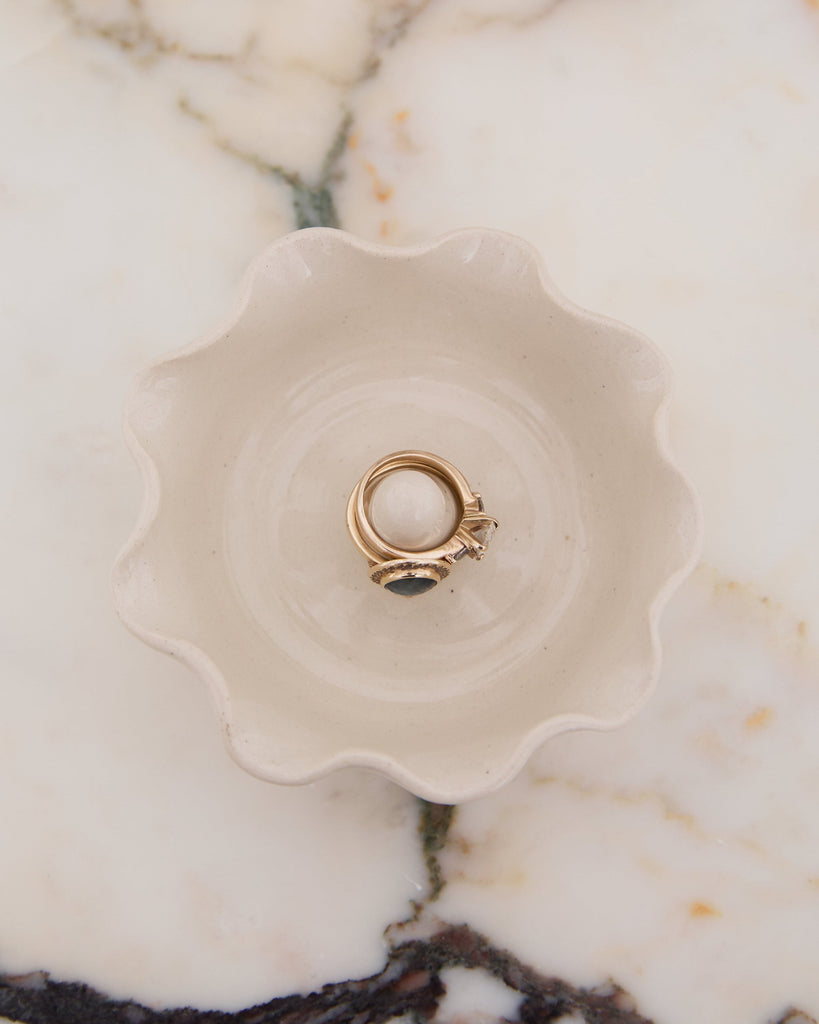 Gold ring with a central gemstone on a decorative ceramic dish against a marble background