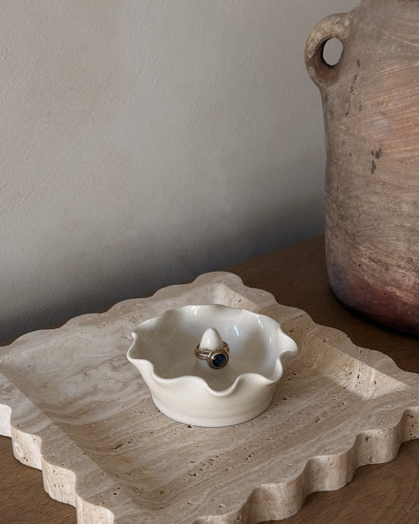 Small white ceramic ring dish with a ring on a textured stone surface.