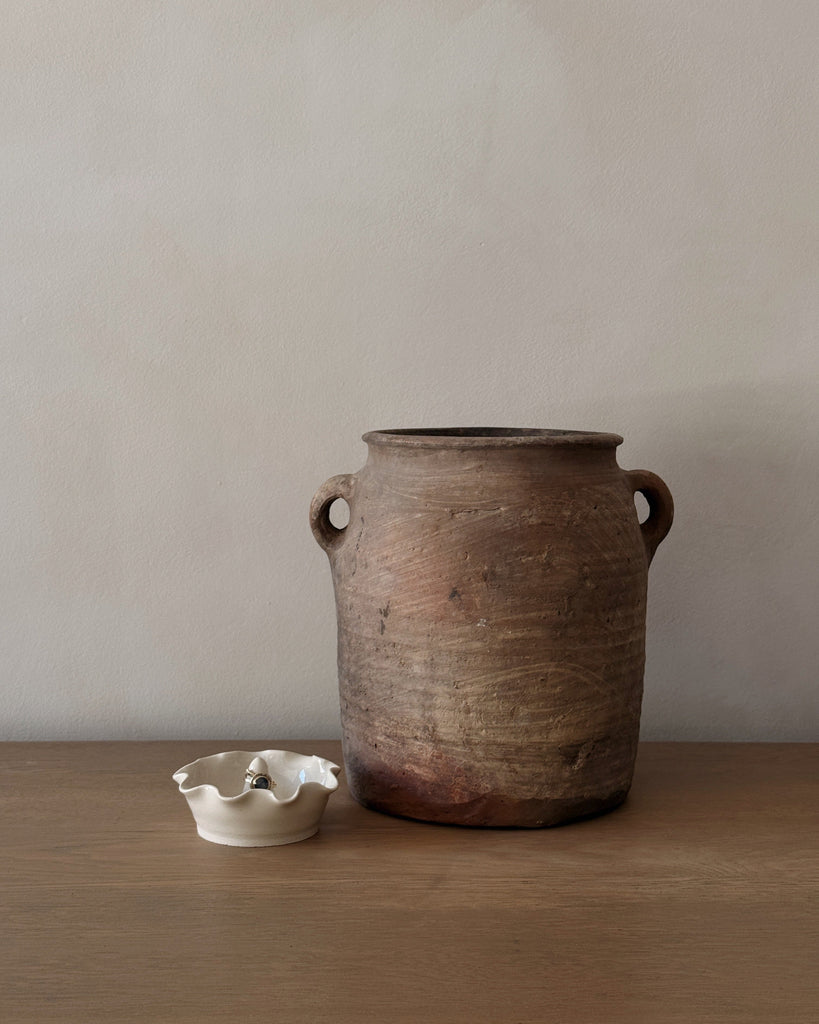 Brown ceramic jar with two handles on a wooden surface against a plain wall.