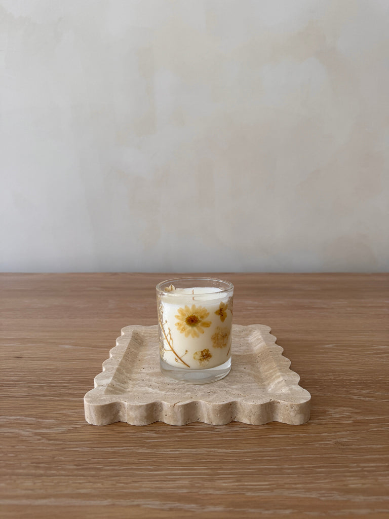 Candle with floral design on a decorative stone travertine tray on a wooden surface