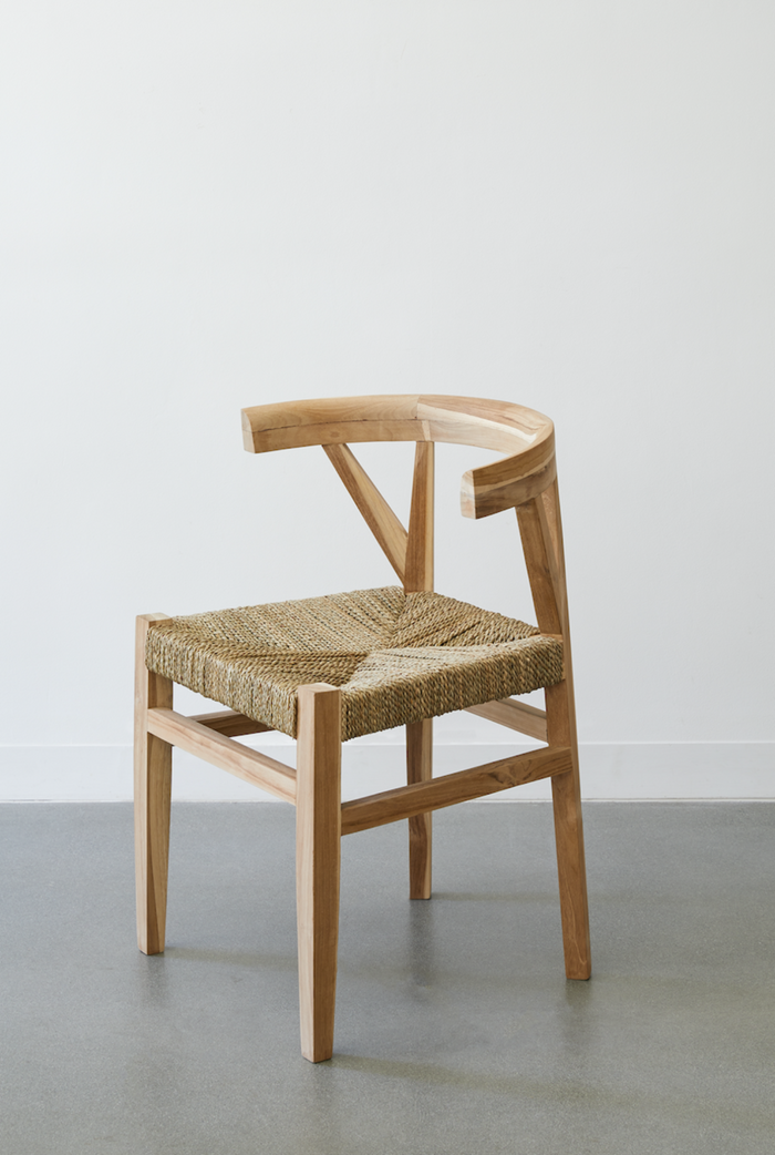 Side view of the Rattan Curved Back Dining Chair against a white background and concrete floors. - Saffron and Poe