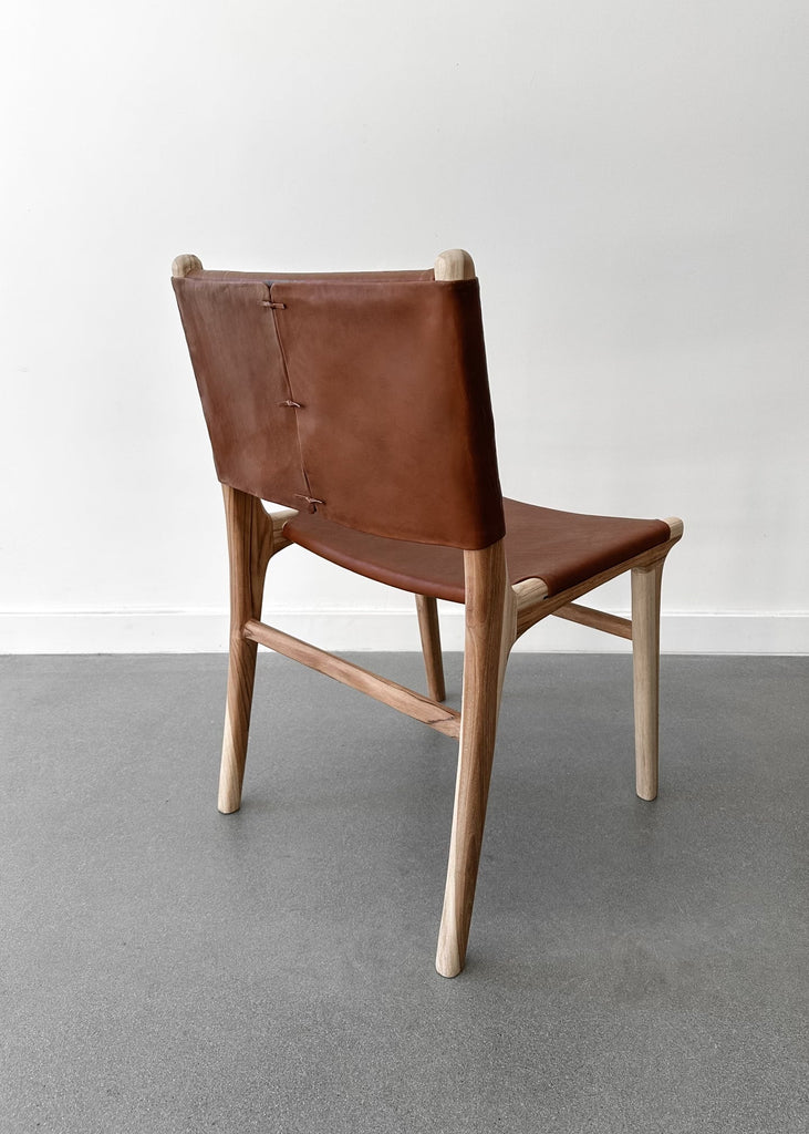 Back of our Stretched Leather and Teak Wood Sofía Dining Chair shot at an angle with a white background. - Saffron + Poe