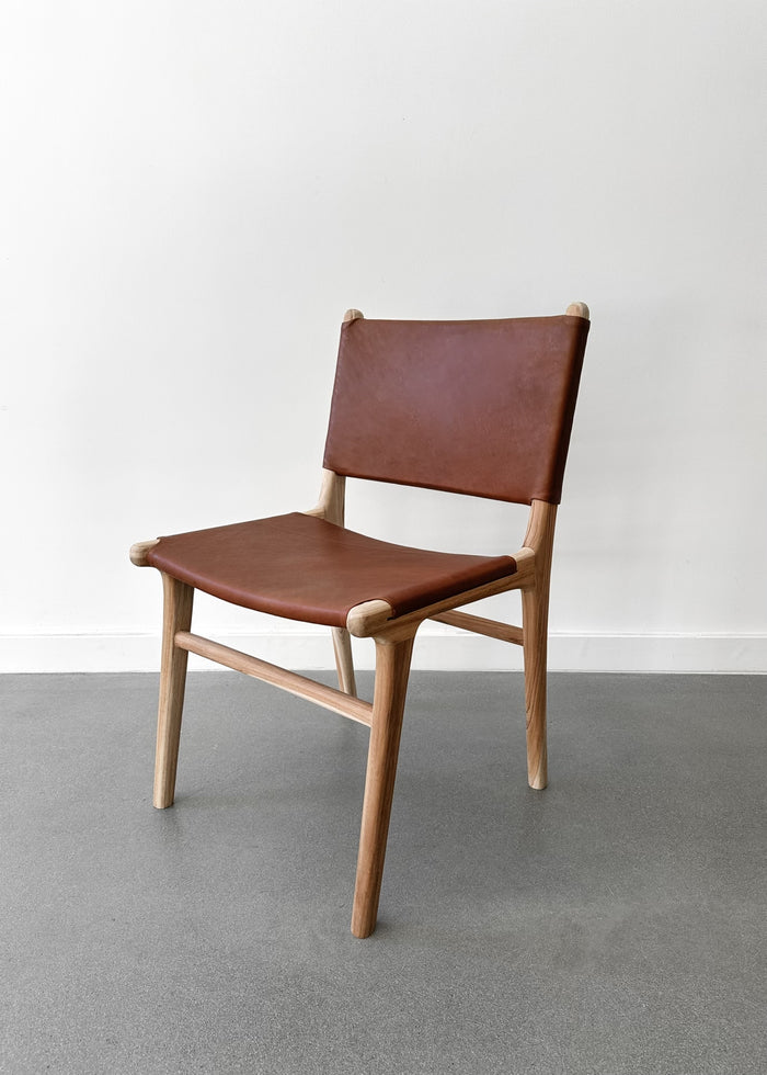 Our Stretched Leather and Teak Wood Sofía Dining Chair shot at an angle with a white background. - Saffron + Poe