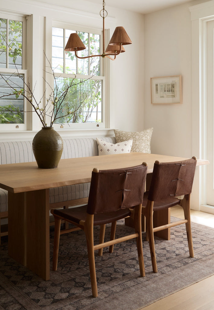 Dining nook with white oak table and Sofia wrapped leather chairs, large window, and decorative elements. Saffron + Poe