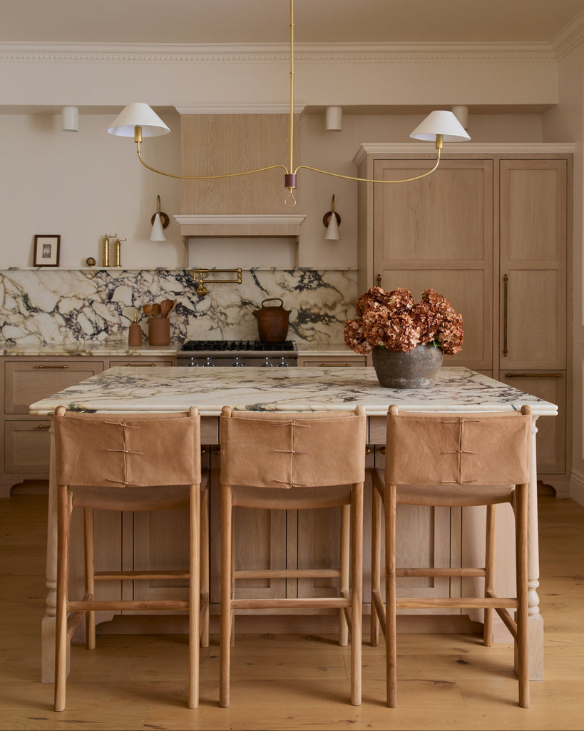Smooth Leather and Teak Sofia Counter stool with back ties in marble kitchen with white oak cabinets and floors. Saffron and Poe