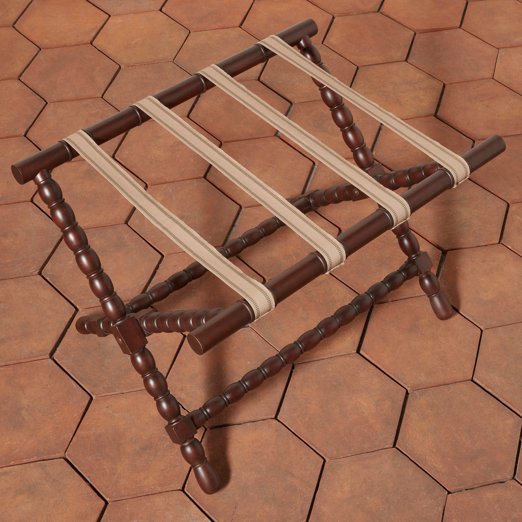 Top view of Somerset Luggage Rack with dark brown bobbin turned-spindle legs and beige cotton straps, shown on a terracotta hexagonal tile floor.