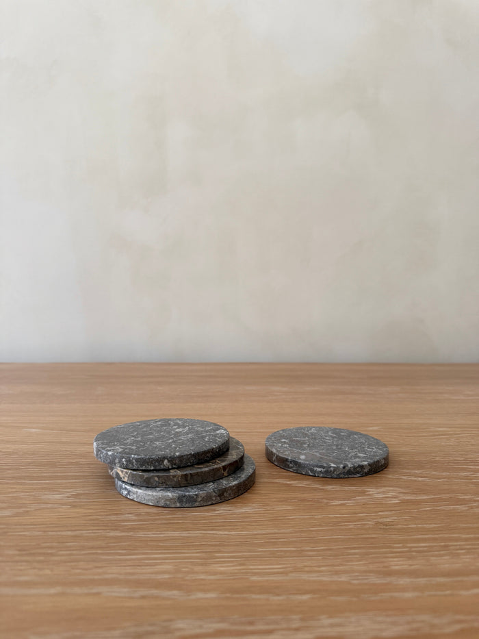 Three dark grey stone coasters on a wooden surface with a plain background