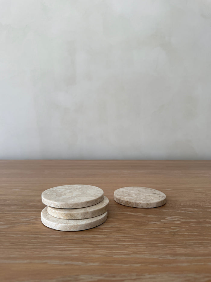 Stack of round ivory colored stone coasters on a wooden surface with a plain background