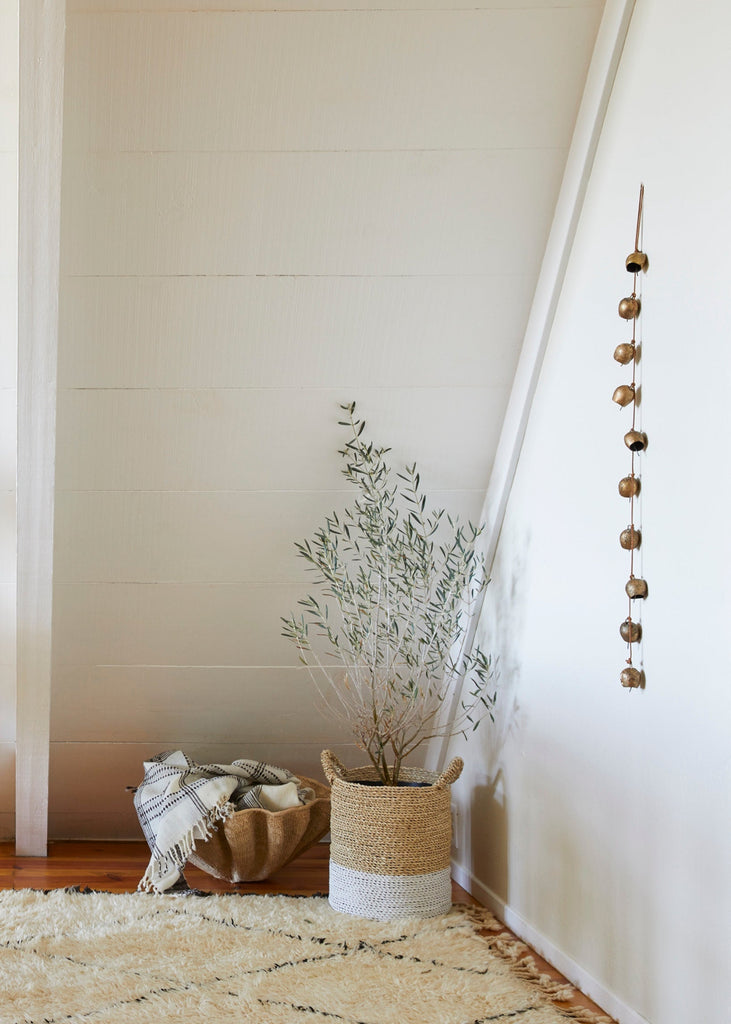 Room interior with a plant, basket, and vintage string of bells hanging on a white wall.