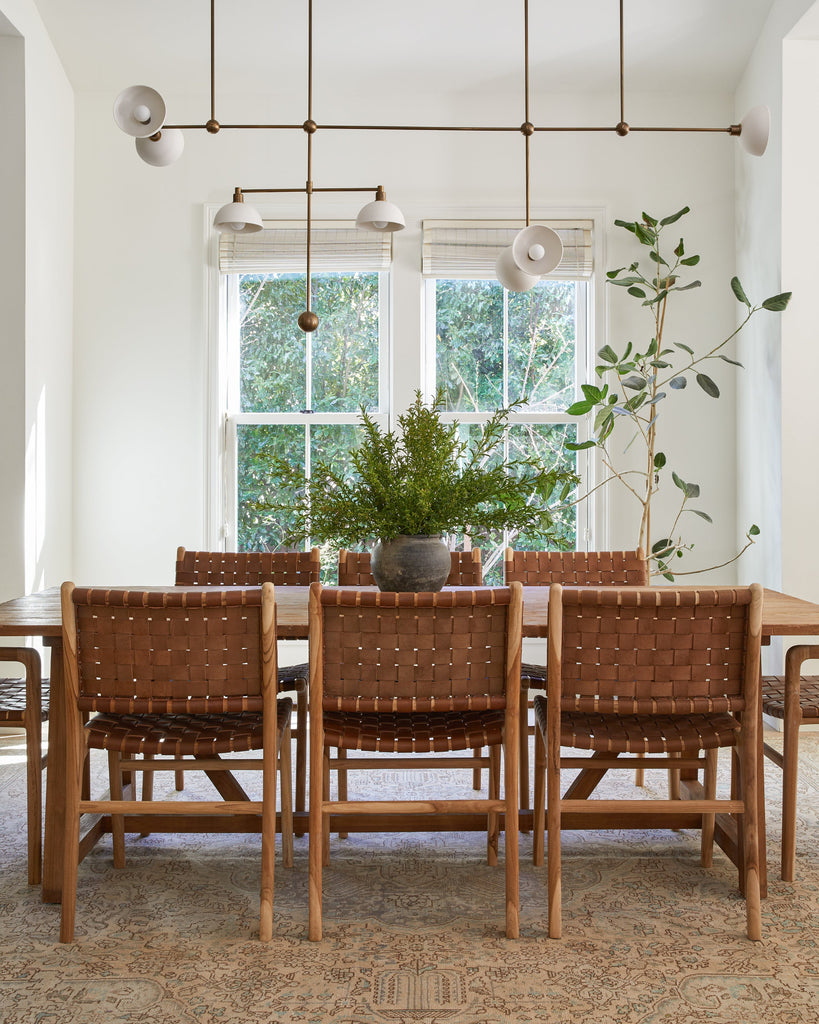 Woven Leather Dining Chair in Saddle leather at dining table with Turkish rug and modern chandelier.