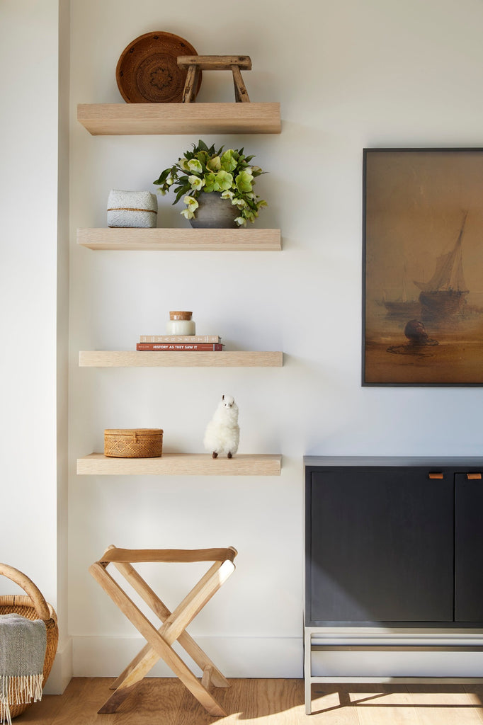 Styled photo of Leather Folding Stool in a living room setting with floating shelves that include Beaded Bali Basket, Antique Clay Pot, Petit Stool, and Alpaquita. - Saffron and Poe