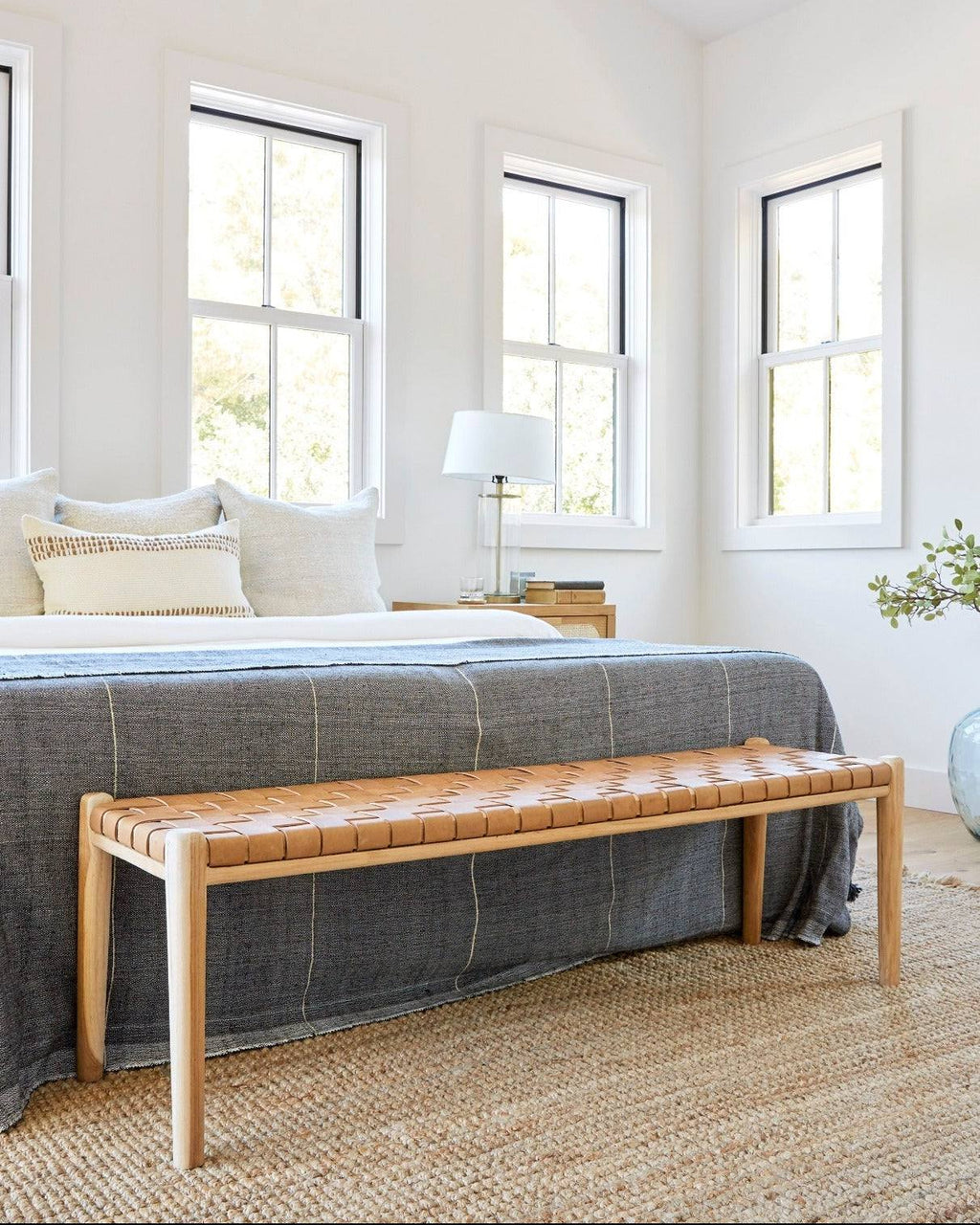 Beige woven leather bench with teak frame and mid-century turned legs in bright bedroom