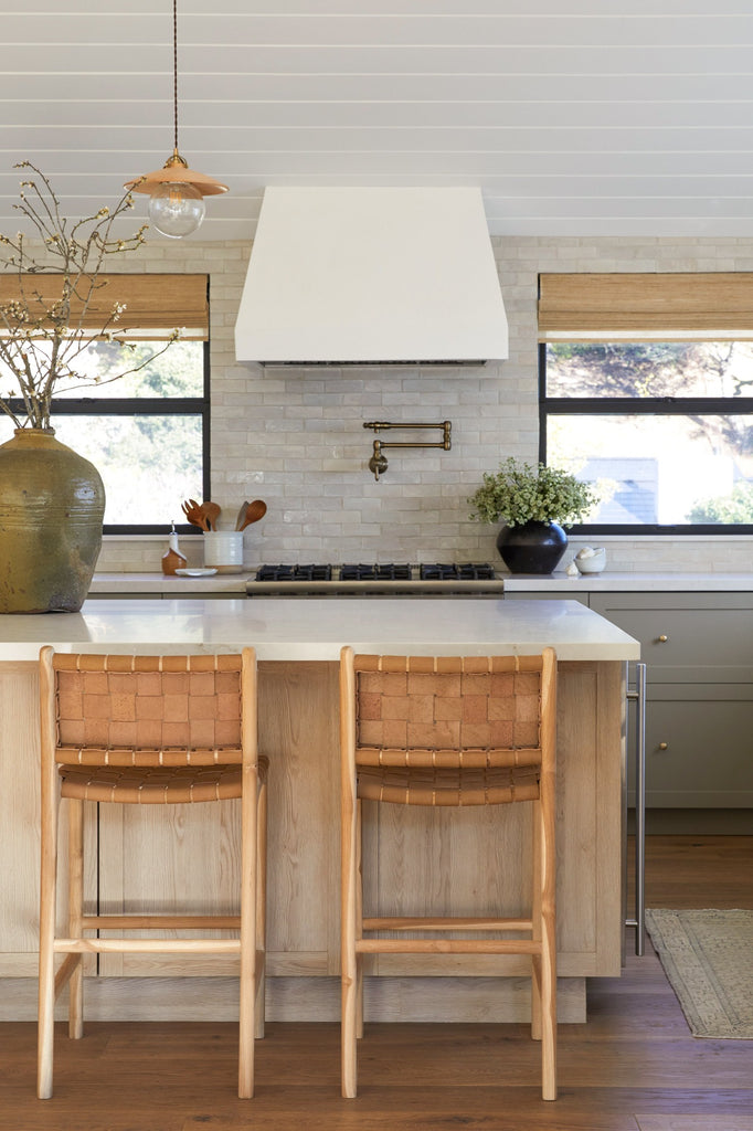 Woven Leather Counter Stool in Beige styled in a kitchen setting with Antique Clay Pot, Vintage Mijiu Jar, Ceramic Utensil Jar, and Ceramic Olive Oil Bottle. -Saffron and Poe 