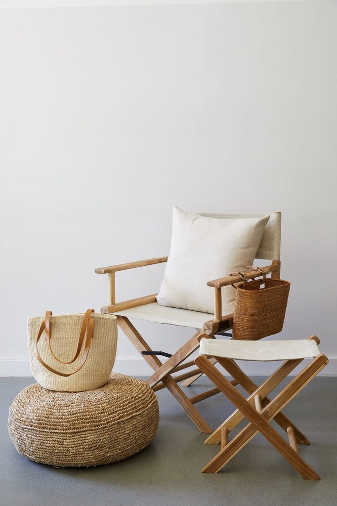  Side view of Oatmeal Director's Chair and Oatmeal Canvas Folding Stool against white wall with Tenganan Side Basket and Natural Woven Pouf. - Saffron and Poe