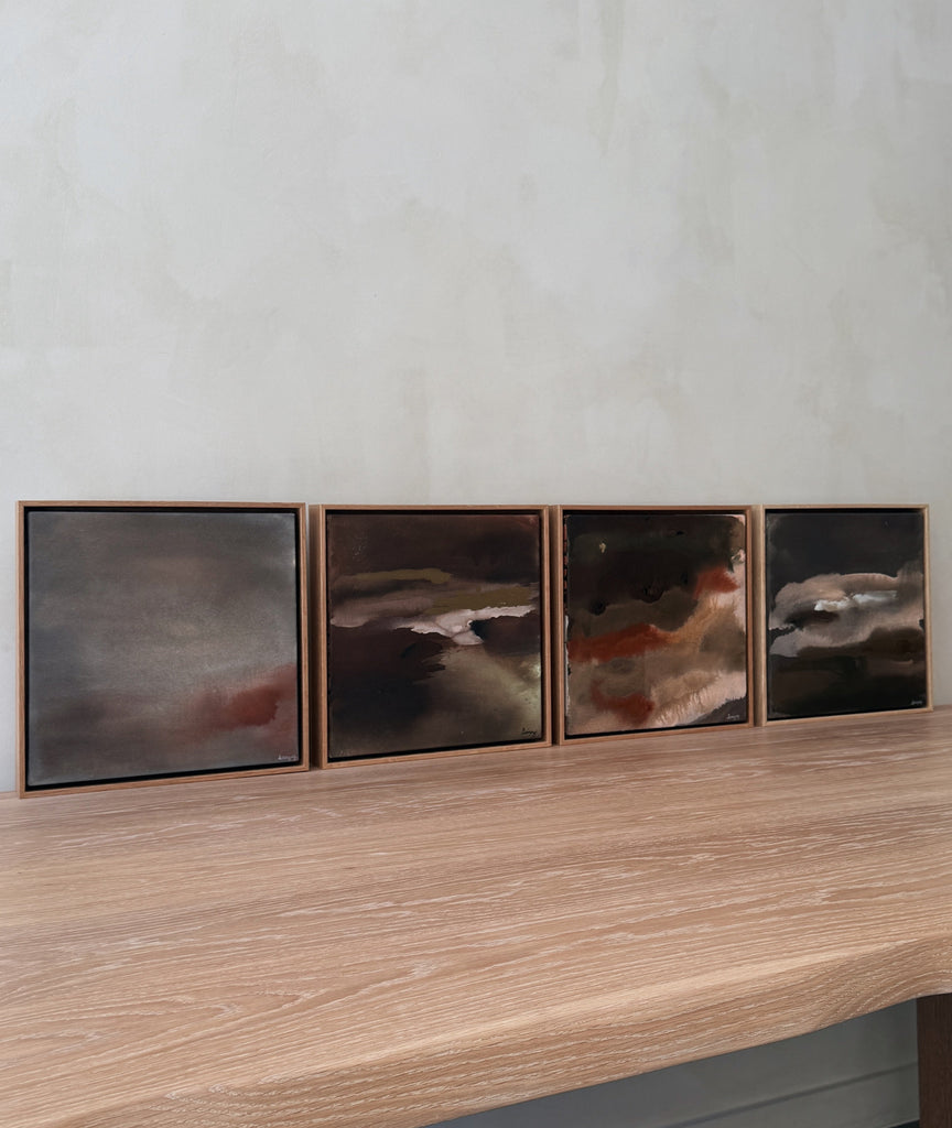 Four framed abstract paintings on a wooden surface with a neutral background