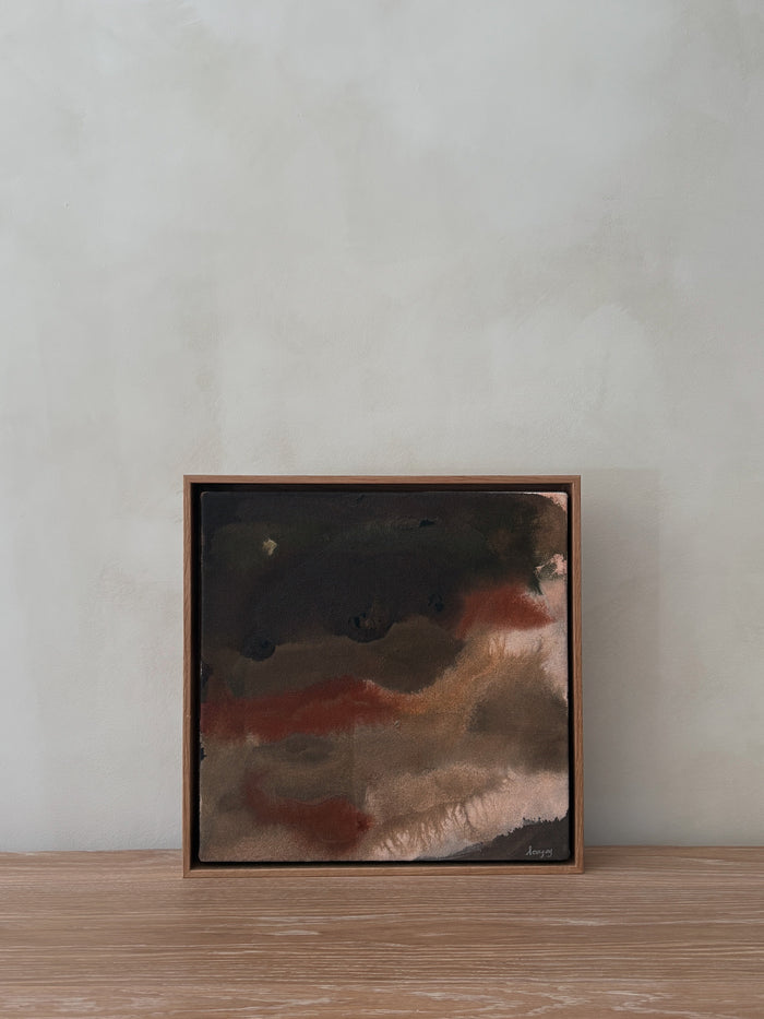 Framed abstract painting on a wooden surface with a neutral wall background