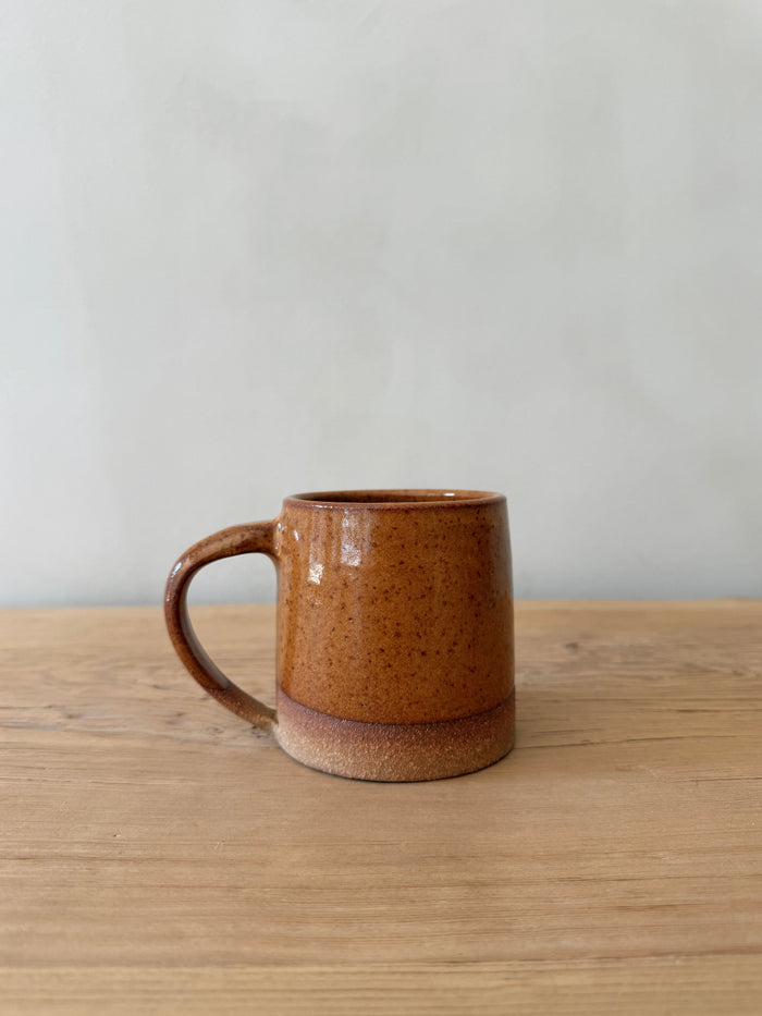 Brown ceramic mug on a wooden surface with a plain background. Saffron + Poe