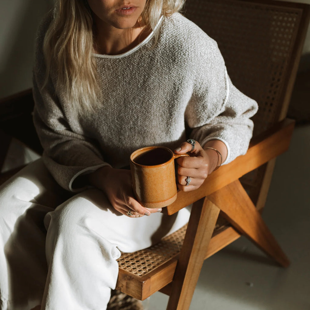 Person sitting on a wooden chair holding a wooden mug in a warm, indoor setting.