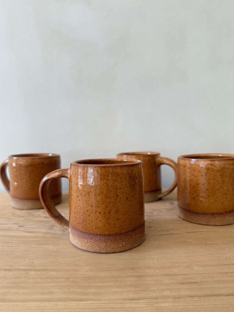 Set of four brown ceramic mugs on a wooden surface with a white background. Saffron + Poe