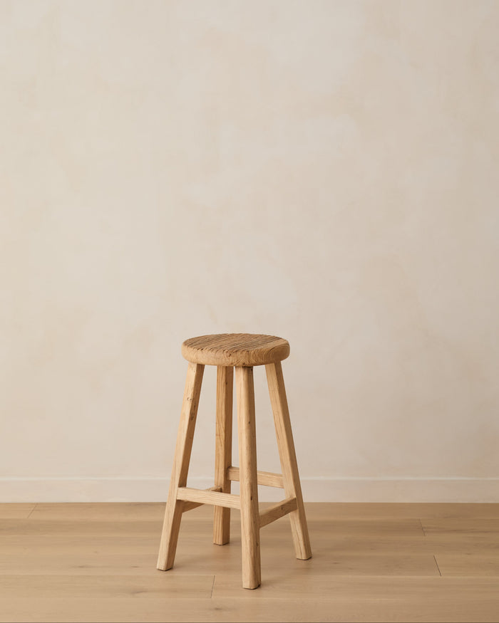 Vintage Reclaimed Elmwood Counter Stool angled against beige lime washed wall and oak floor.