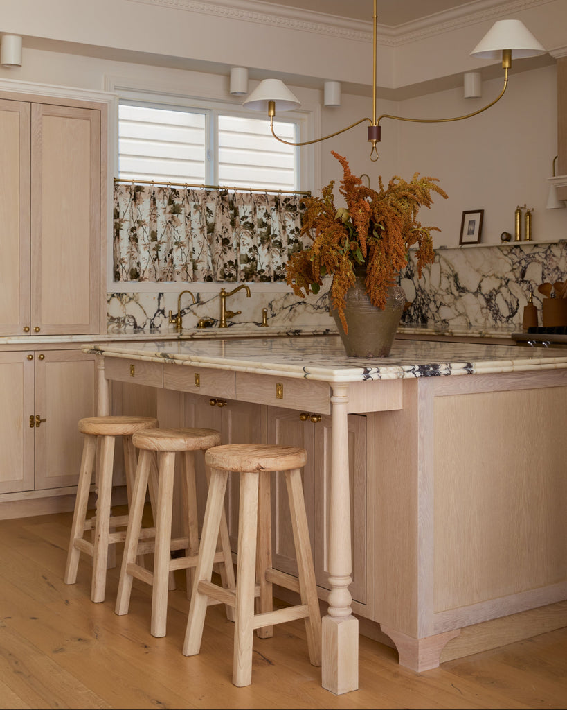 Modern but timeless kitchen with angled vintage elmwood counter stools at an island light wood cabinets, and marble countertop. 