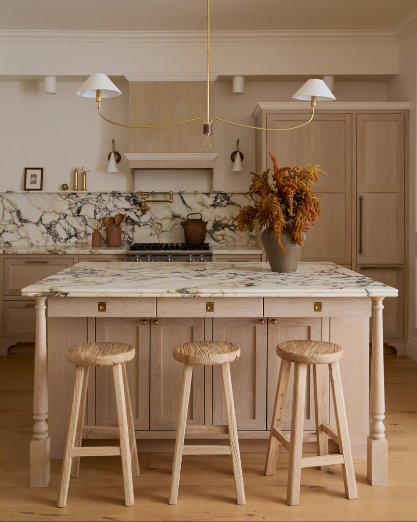 Modern kitchen with vintage elmwood counter stools at an island, light wood cabinets, and marble countertop. 