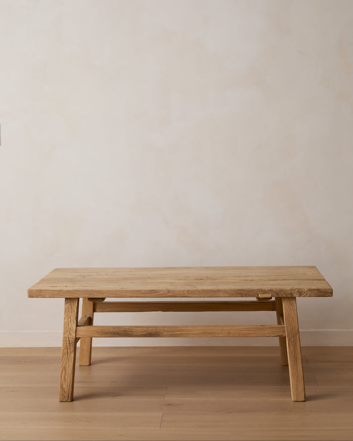 Vintage light elm Wood Coffee Table with a thick rectangular top and four sturdy legs, set against a neutral beige plaster wall and light wood floor.