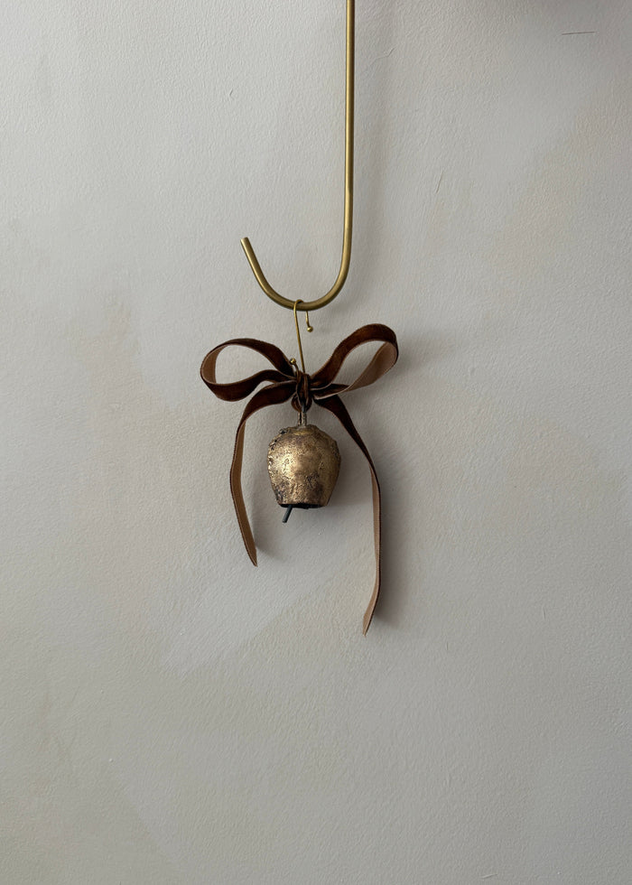 Small brass bell ornament with a brown ribbon on a limewash background
