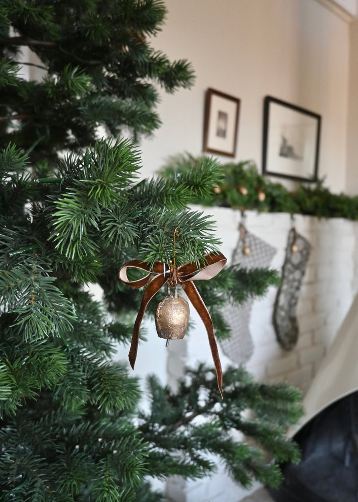 Vintage Brass Bell ornament on a Christmas tree with a fireplace and stockings in the background.