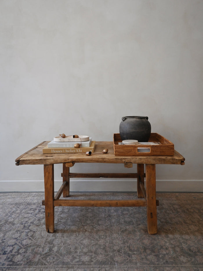 Antique wooden table with a tray holding a pot and other items against a plain wall.