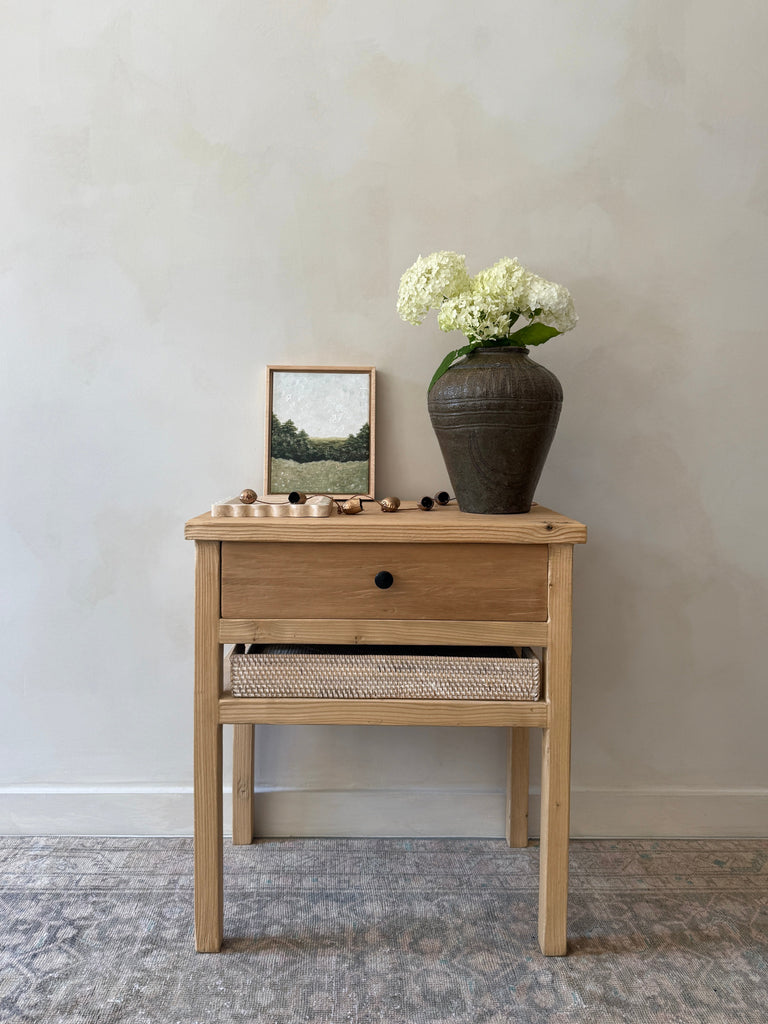 Vintage Reclaimed Elmwood Bedside Table with hammered drawer knob styled with art and an antique vessel in front of beige limewashed wall. Saffron + Poe